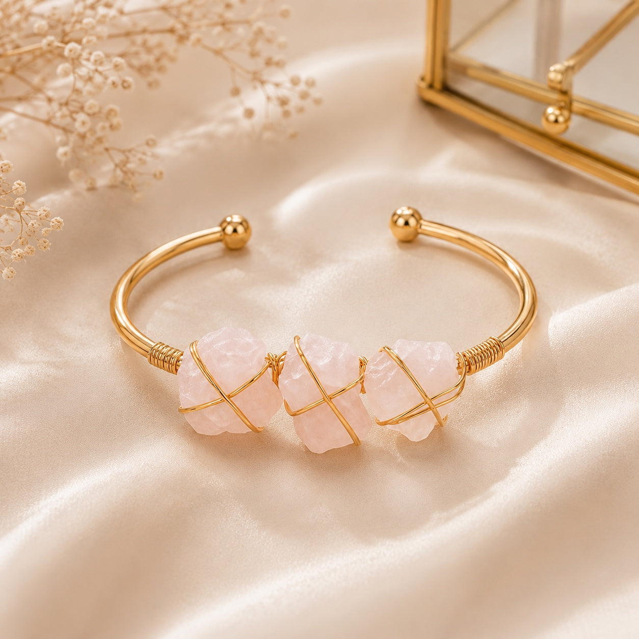 Rose quartz stone cuff bracelet with three pink stones and gold wire on beige fabric.