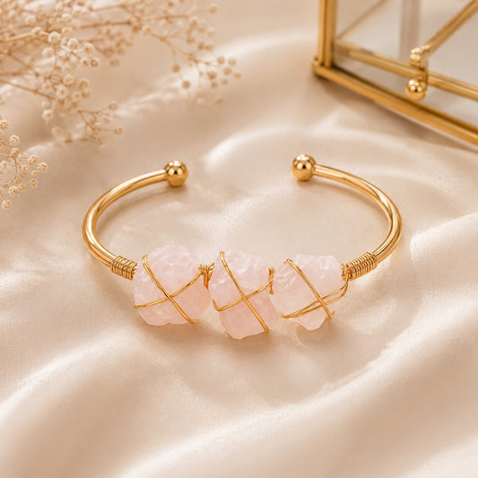 Rose quartz stone cuff bracelet with three pink stones and gold wire on beige fabric.