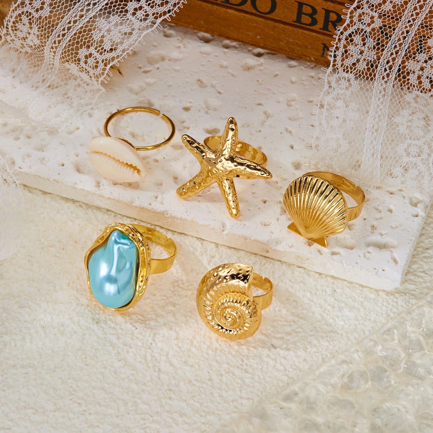 Seaside Treasures Ring Set featuring gold-tone starfish, seashell, cowrie shell, spiral shell, and aqua statement rings in a coastal-inspired display.