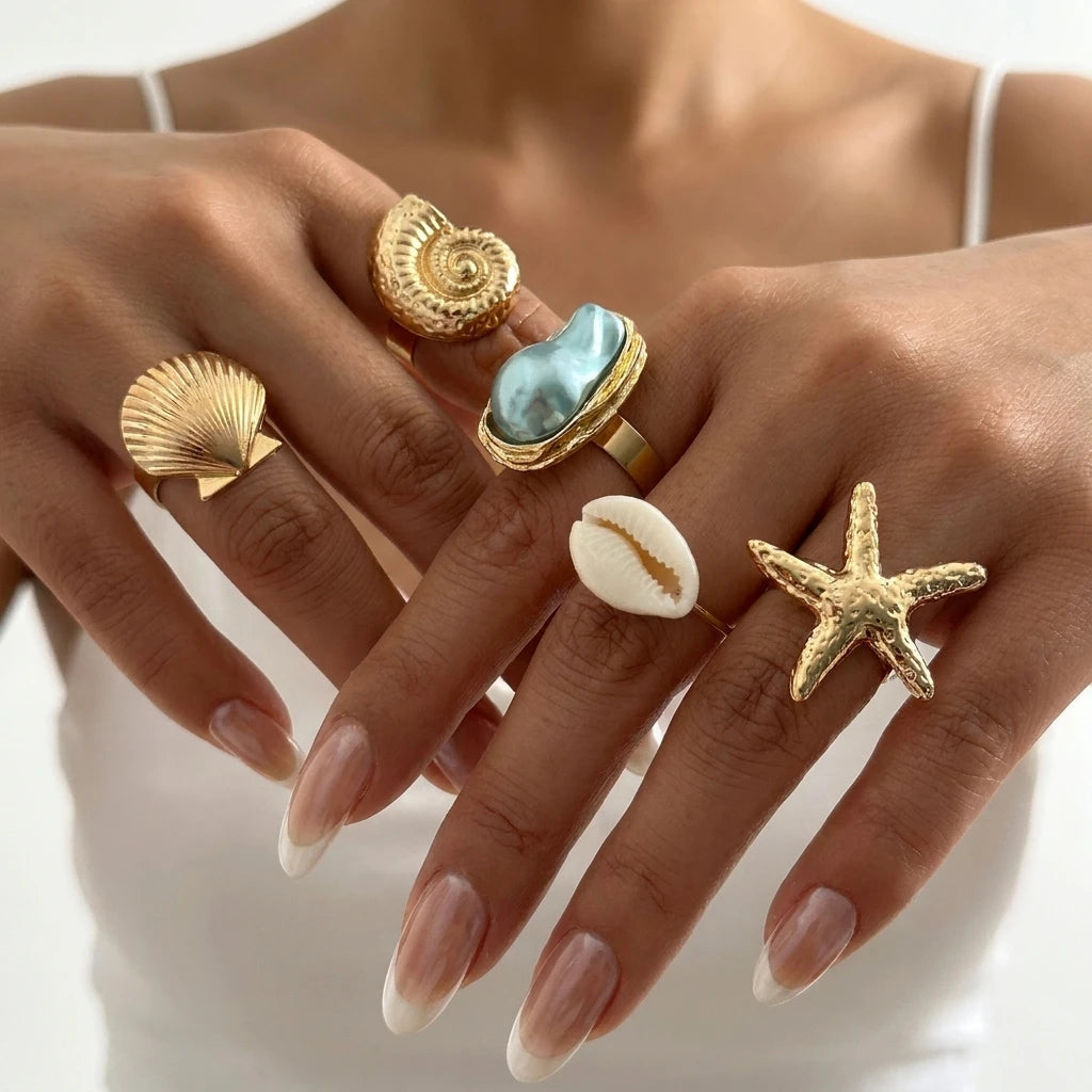 Seaside Treasures Ring Set featuring gold-tone starfish, seashell, cowrie shell, and aqua statement rings worn by a model.