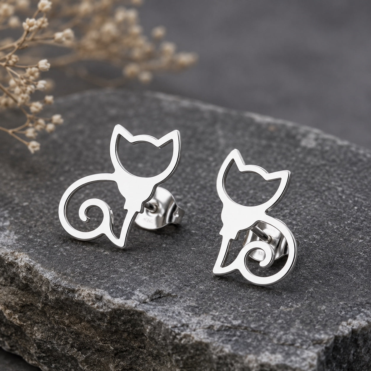 Close-up of silver cat stud earrings with a minimalist cat silhouette design on a dark stone display.