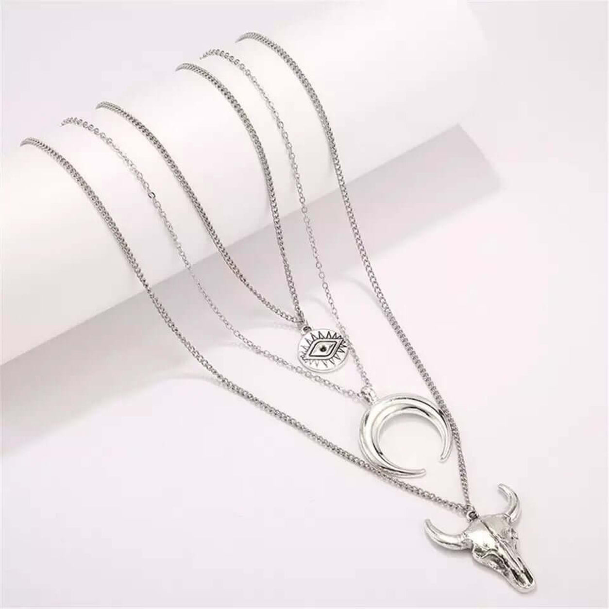 Silver Layered Boho Necklace displayed in a flat lay with layered chains, evil eye charm, crescent horn, and bull skull pendants.