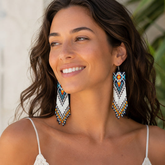 Woman wearing colorful Southwest beaded fringe earrings with geometric tribal pattern and long white beaded tassels.