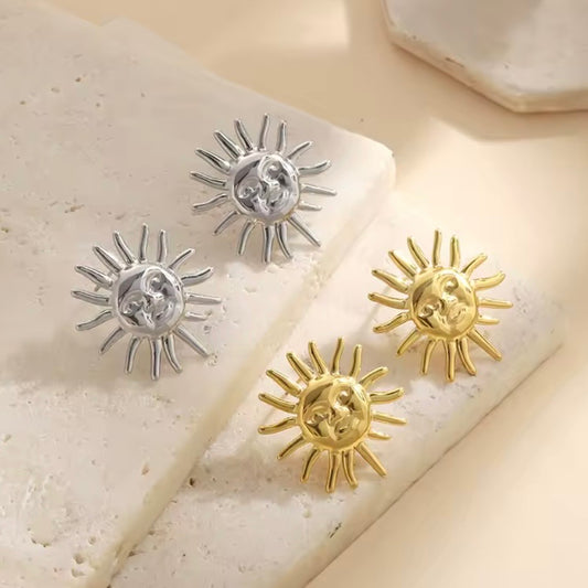 Sun Goddess Stud Earrings shown in gold and silver finishes on a neutral stone background.