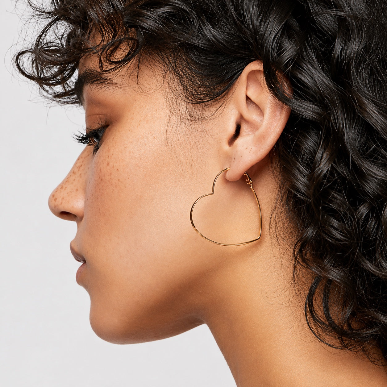 Woman wearing Timeless Heart Hoop Earrings in a close-up side profile.