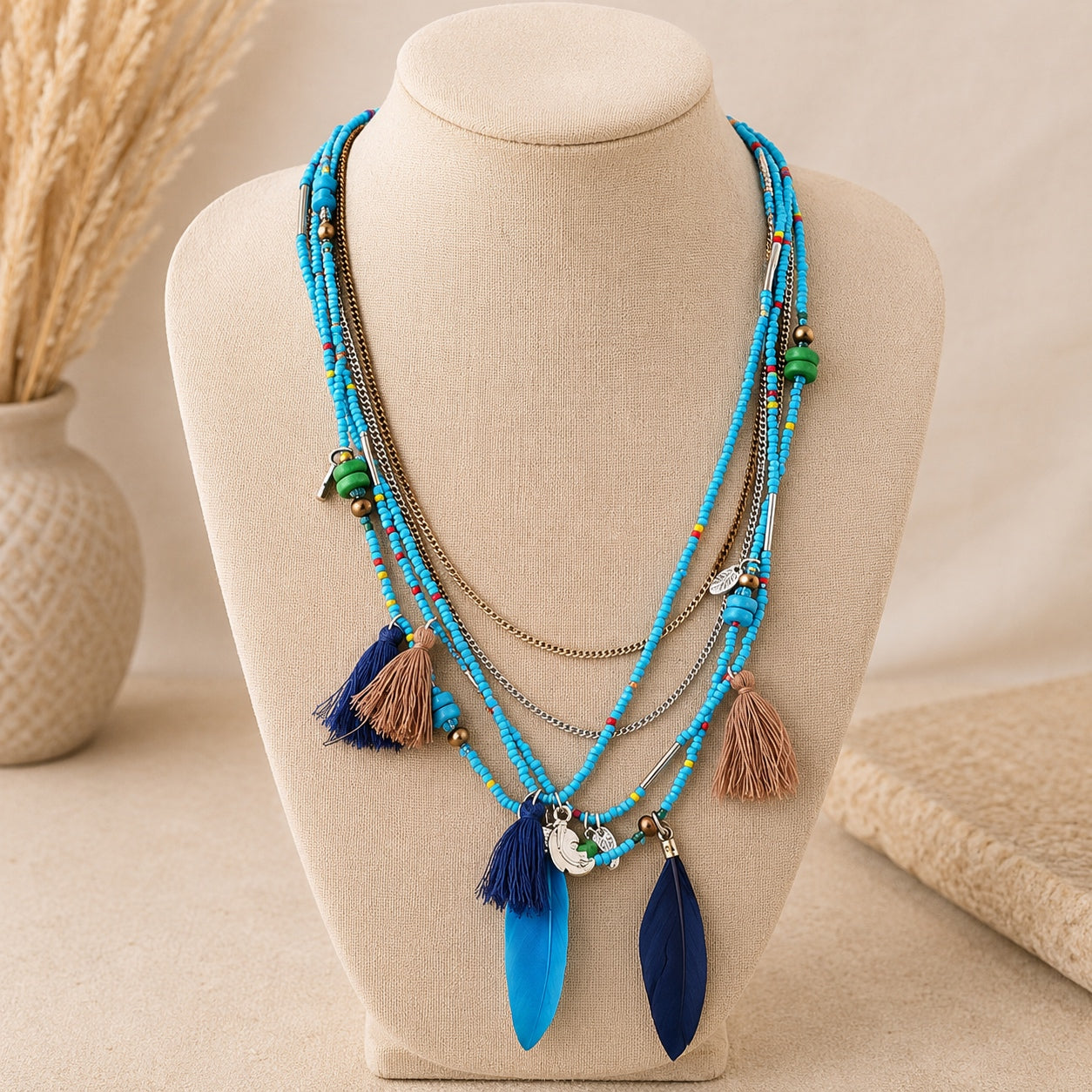 Turquoise layered boho beaded necklace with blue feather pendants, tassels and mixed metal chains displayed on a linen jewelry bust.