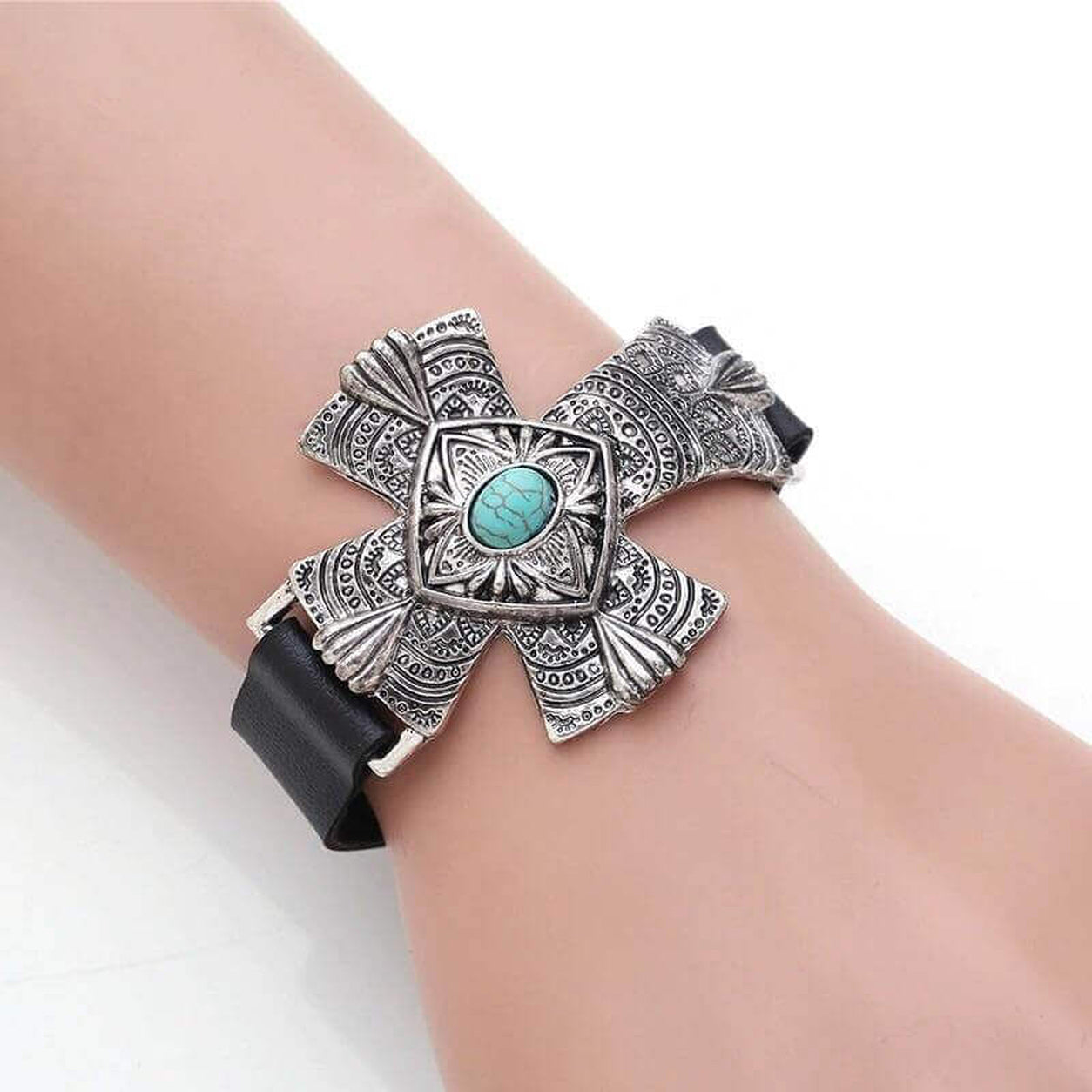 Woman wearing the Turquoise Cross Statement Bracelet with an engraved silver cross and turquoise stone on a black leather band.