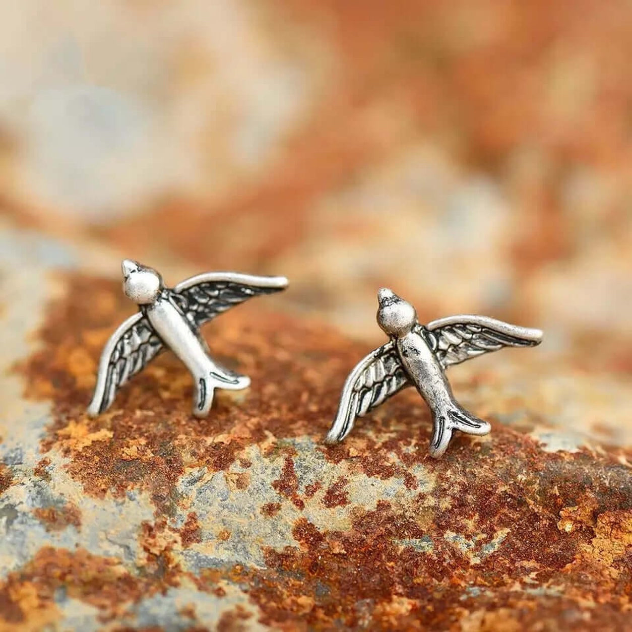 Vintage Silver Bird Stud Earrings with detailed wings displayed on a rustic textured background.