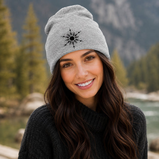 Woman wearing the Wanderlust Snowflake Beanie Hat in Heather Gray featuring a black snowflake-inspired Wanderlust design, styled outdoors in a scenic mountain setting.