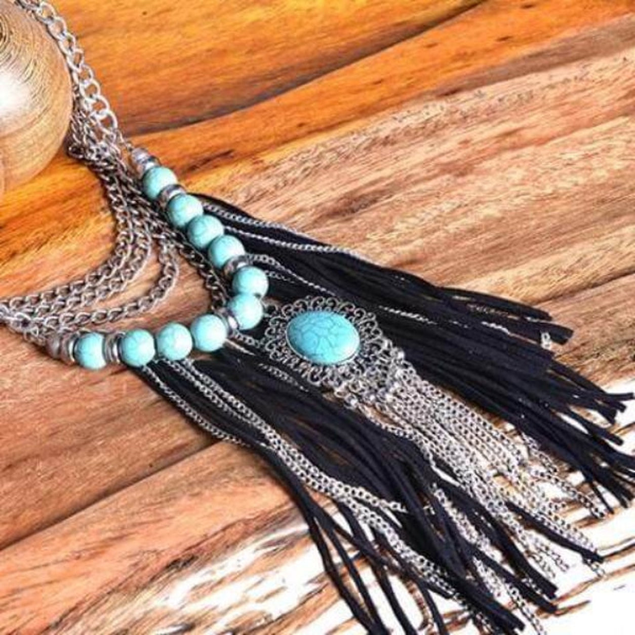 Flat lay of the Western Turquoise Fringe Necklace with silver chains, turquoise stone beads and black suede fringe.