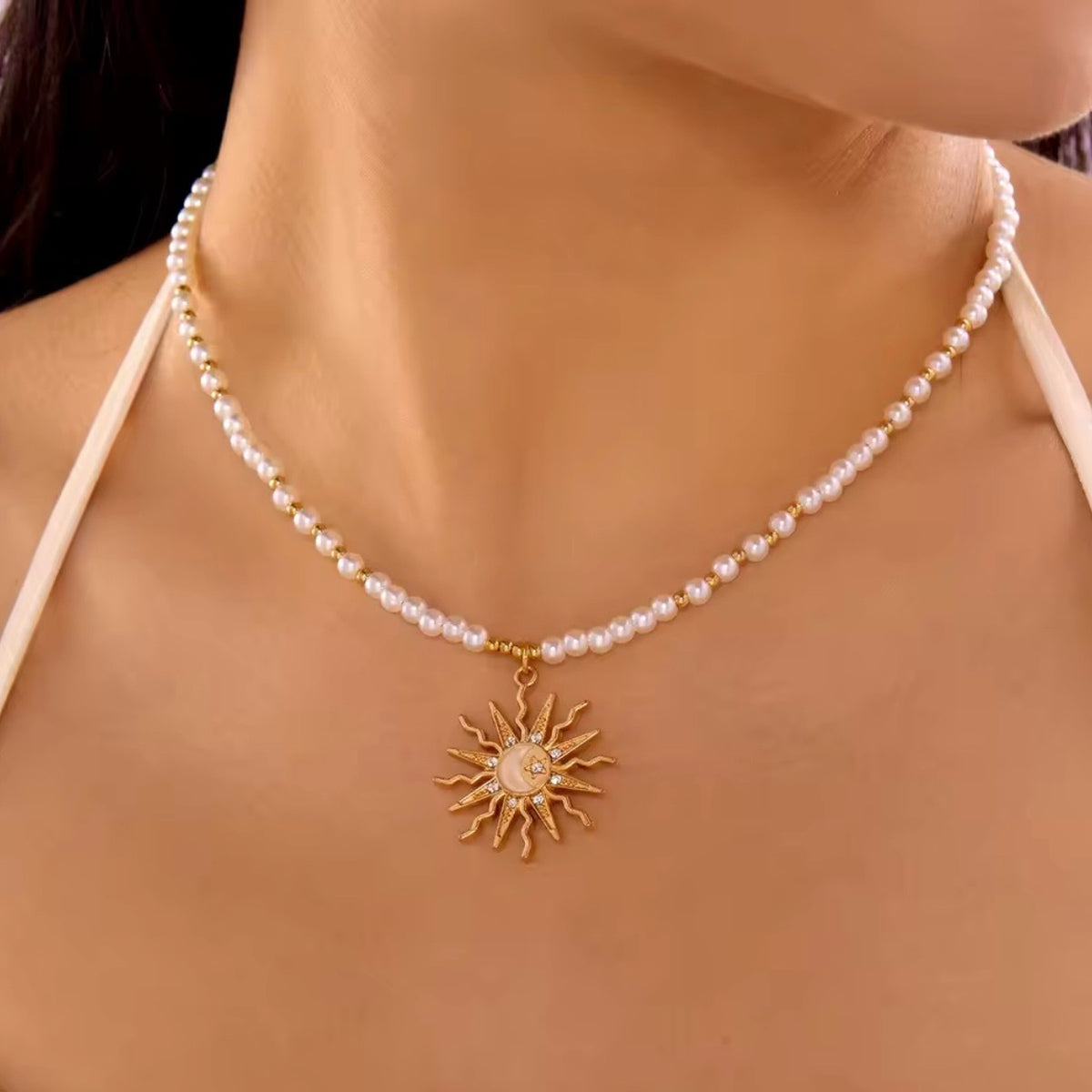 White pearl-style beaded necklace with gold spacer beads and a celestial sun pendant, modeled on the neck.