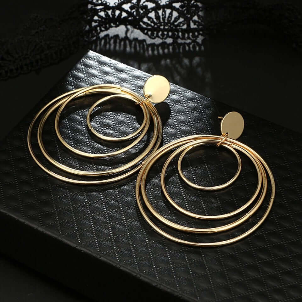 Golden Circles Dangle Earrings displayed on a black textured surface highlighting the layered gold circle design.